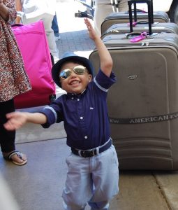 Small child wearing sunglasses and a hat dancing in front of suitcases