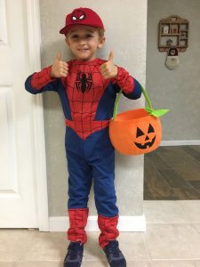 Child in Spider-Man costume with Halloween candy bucket posing with thumbs up