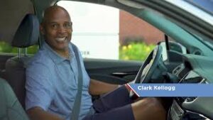 Clark Kellogg behind the driver's seat of a car.