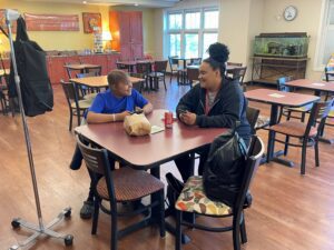 child with IV pole sitting at table with adult