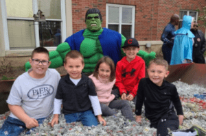 kids sitting in pile of pull tabs smiling with volunteer dressed as hulk.