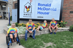 Four children, one in wheelchair, sitting on brick wall with Ronald McDonald House sign