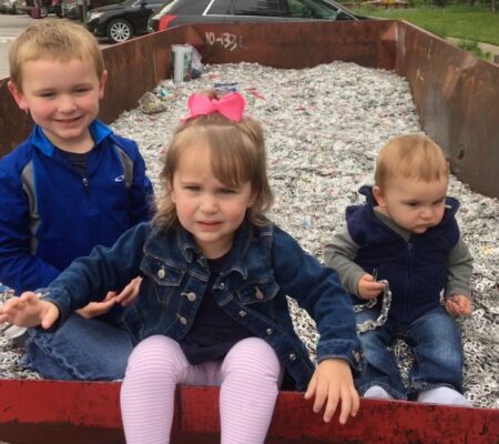 3 children in a recycling bin of pull tabs