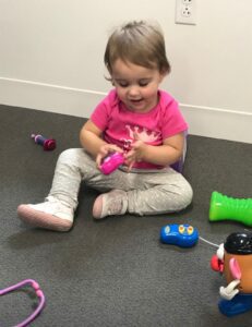 Two-year-old girl in pink shirt sitting pm floor playing with toys on