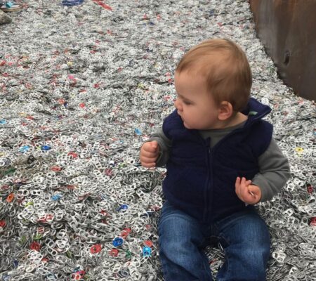 One-year-old boy seated in pull tab recycling bin