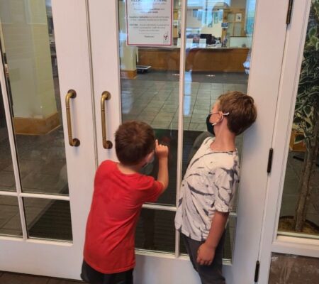 two boys with masks look in closed doors to Ronald McDonald House