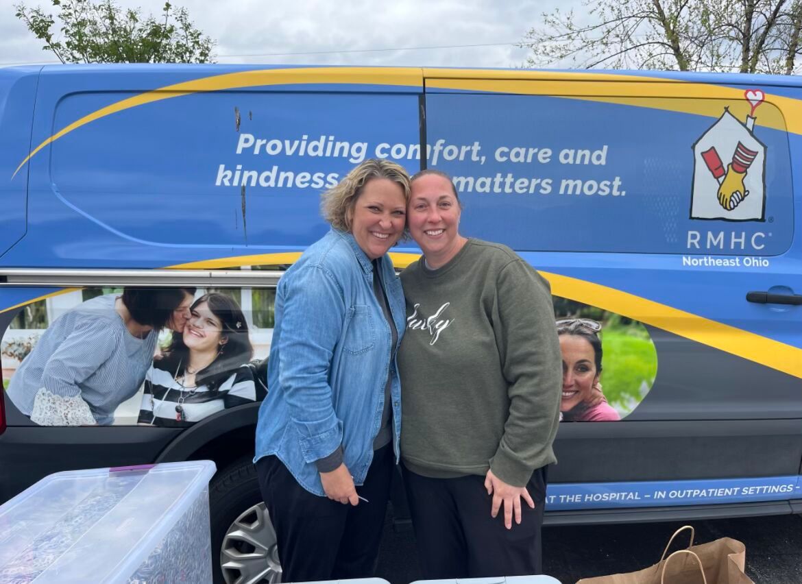 two women hug and pose with van