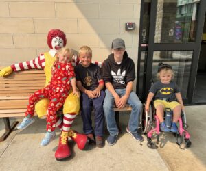 Three children on bench with Ronald McDonald, one in wheelchair