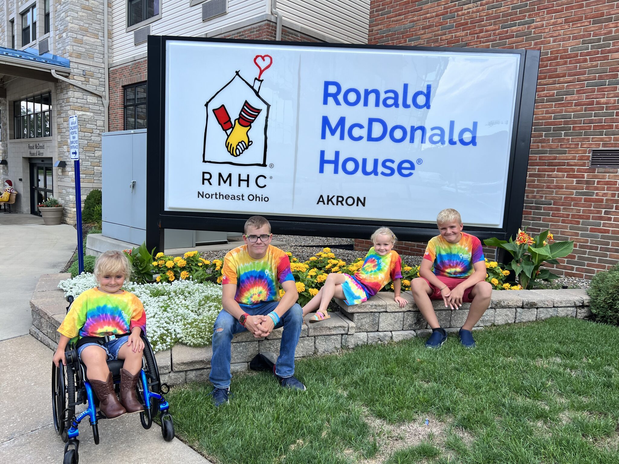 Four children, one in wheelchair, sitting on brick wall with Ronald McDonald House sign