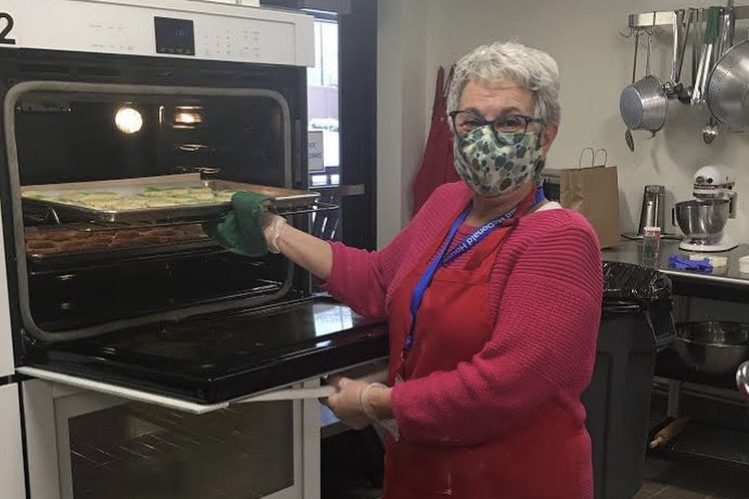 Volunteer wearing face mask pulling a tray of cookies out of a professional oven
