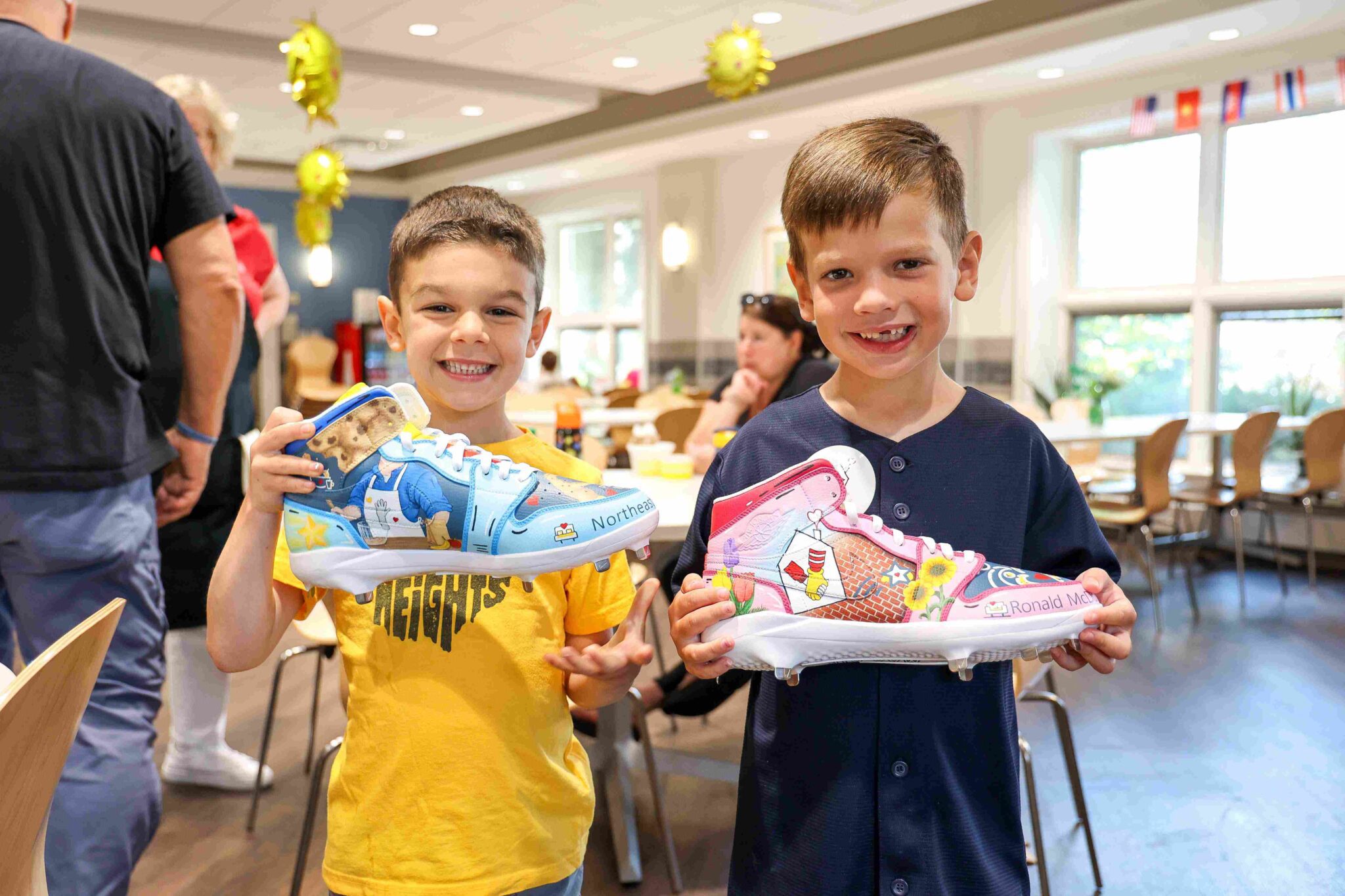 smiling children hold Josh Naylor's custom cleats. They are in a bright sunny room with windows behind them. at the Cleveland Ronald McDonald House