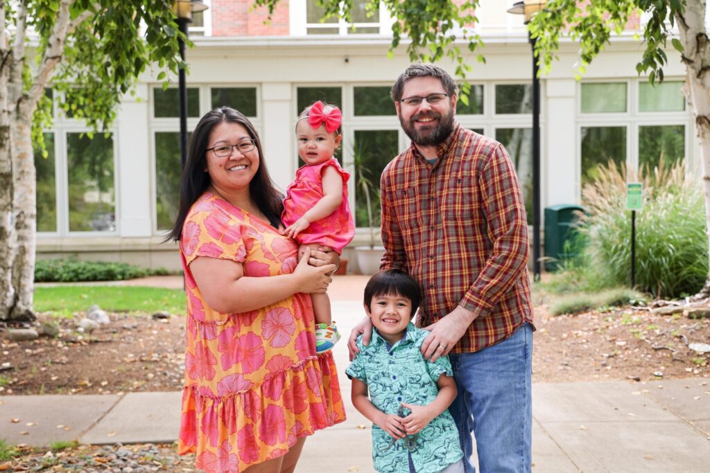 family of four with mom, dad, little boy and baby girl smiling for camera.