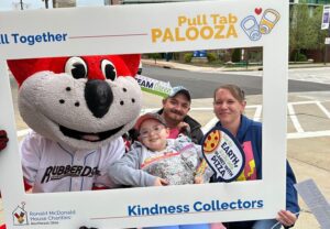 A family poses with a mascot inside a Pull Tab Kindness Collectors frame