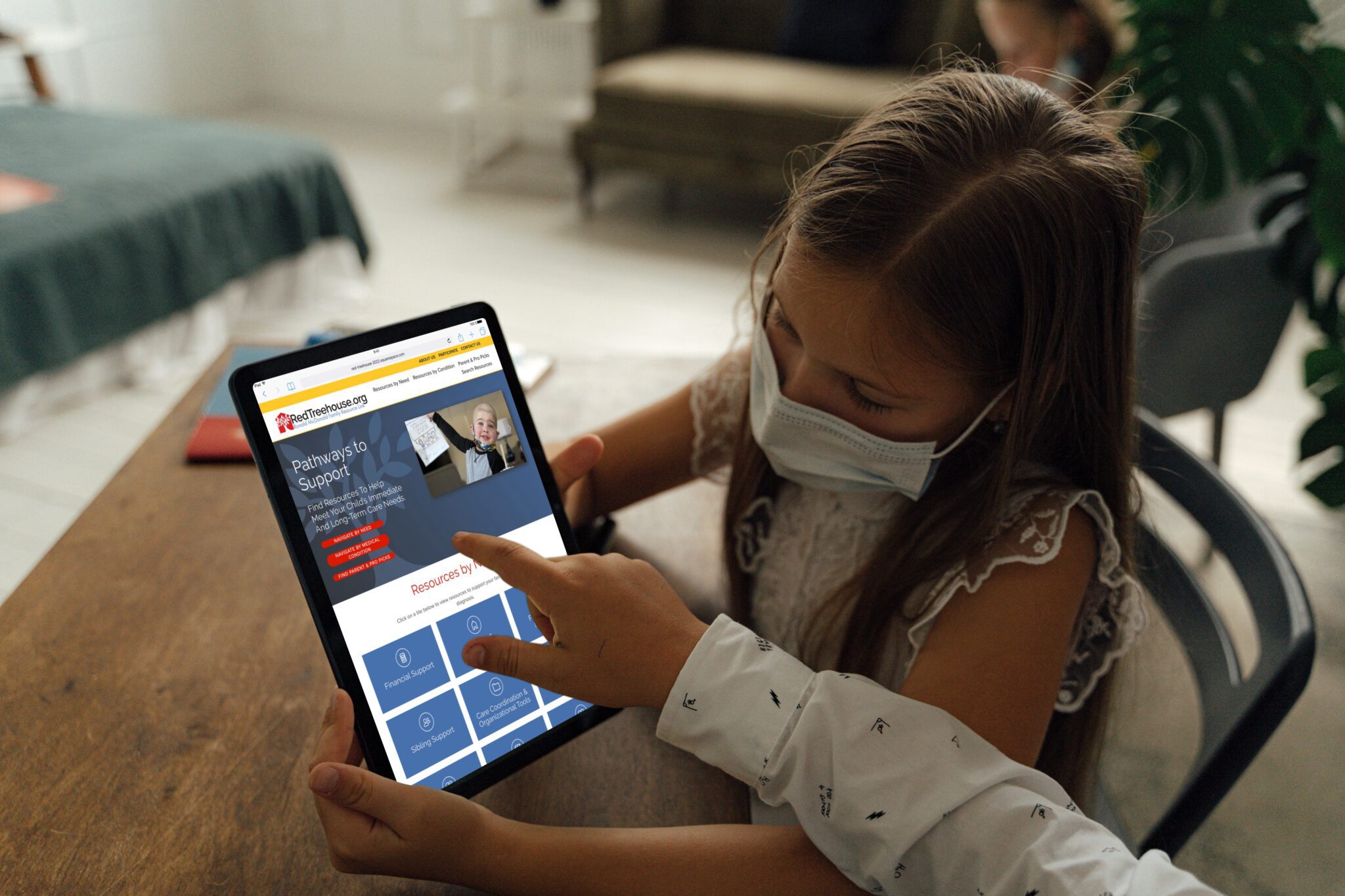 child in mask looking at a tablet with adult pointing at the website displayed