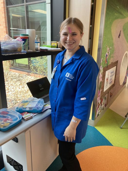 woman in blue volunteer smock standing in pediatric hospital waiting area